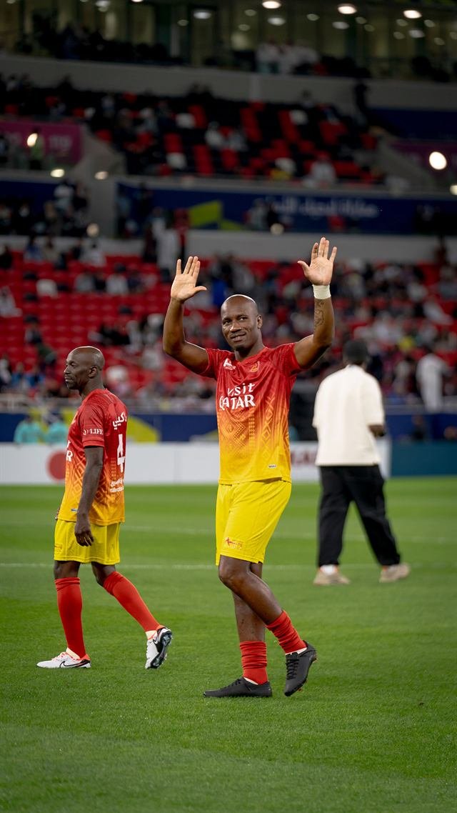 Didier Drogba raises both arms to the crowd in the Visit Qatar kit during Match for Hope in Doha