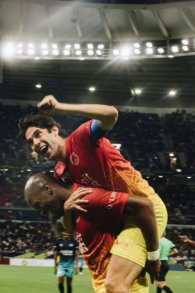 Kaká lifted on a teammate's shoulders, laughing with his fist raised, under the floodlights at Match for Hope in Doha