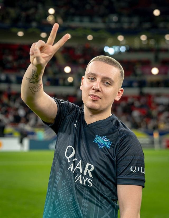 Chunkz in a dark teal Qatar Airways kit holding up a peace sign on the pitch at Match for Hope in Doha