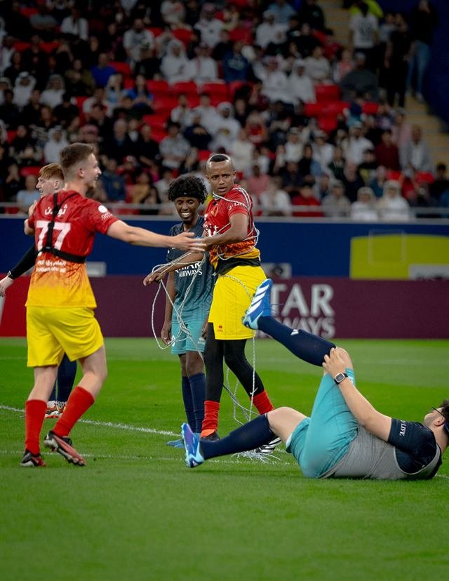 Players laughing on the pitch as one of them stands tangled in a rope and another lies on the grass during Match for Hope in Doha