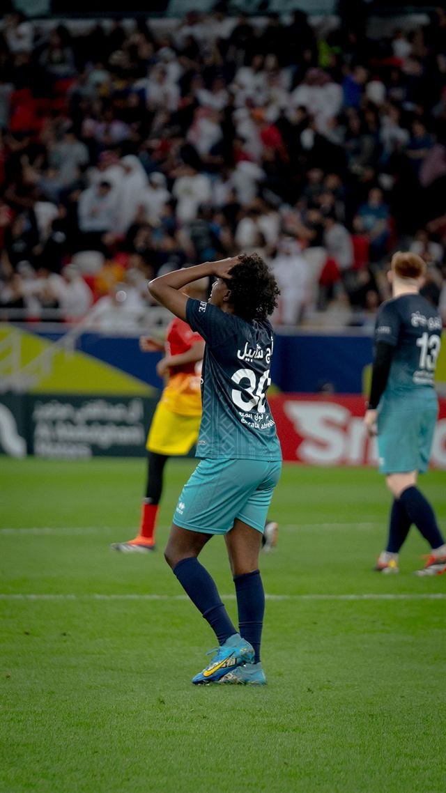 A player in a teal kit stands with his hands on his head after a missed chance on the floodlit pitch at Match for Hope